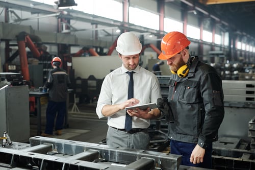 two men in a manufacturing plant looking at a tablet